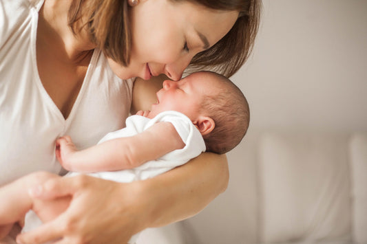 Mother lovingly holding and nuzzling newborn baby wrapped in white cloth on neutral background